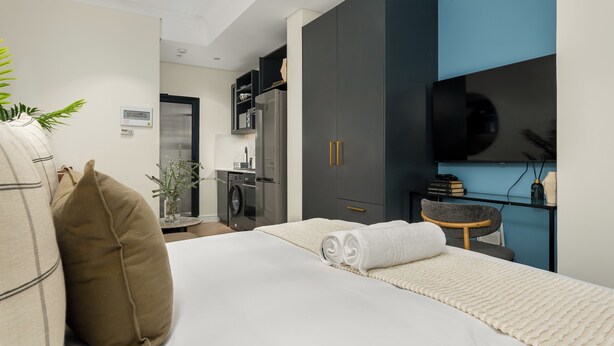 Una habitación de hotel moderna con cama, escritorio, silla, armario, televisión y lavadora.