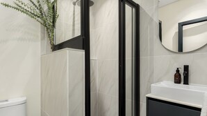 Un baño moderno con ducha de vidrio, un lavabo blanco con gabinete negro y un espejo redondo.