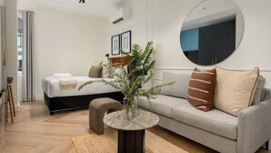 Una habitación de hotel moderna con una cama, un espejo redondo, un sofá y una pequeña mesa redonda con un jarrón.