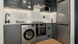 A compact kitchen with a washing machine, oven, and refrigerator. - The Valour Charming Apartment | City and Hill Views (Cape Town)
