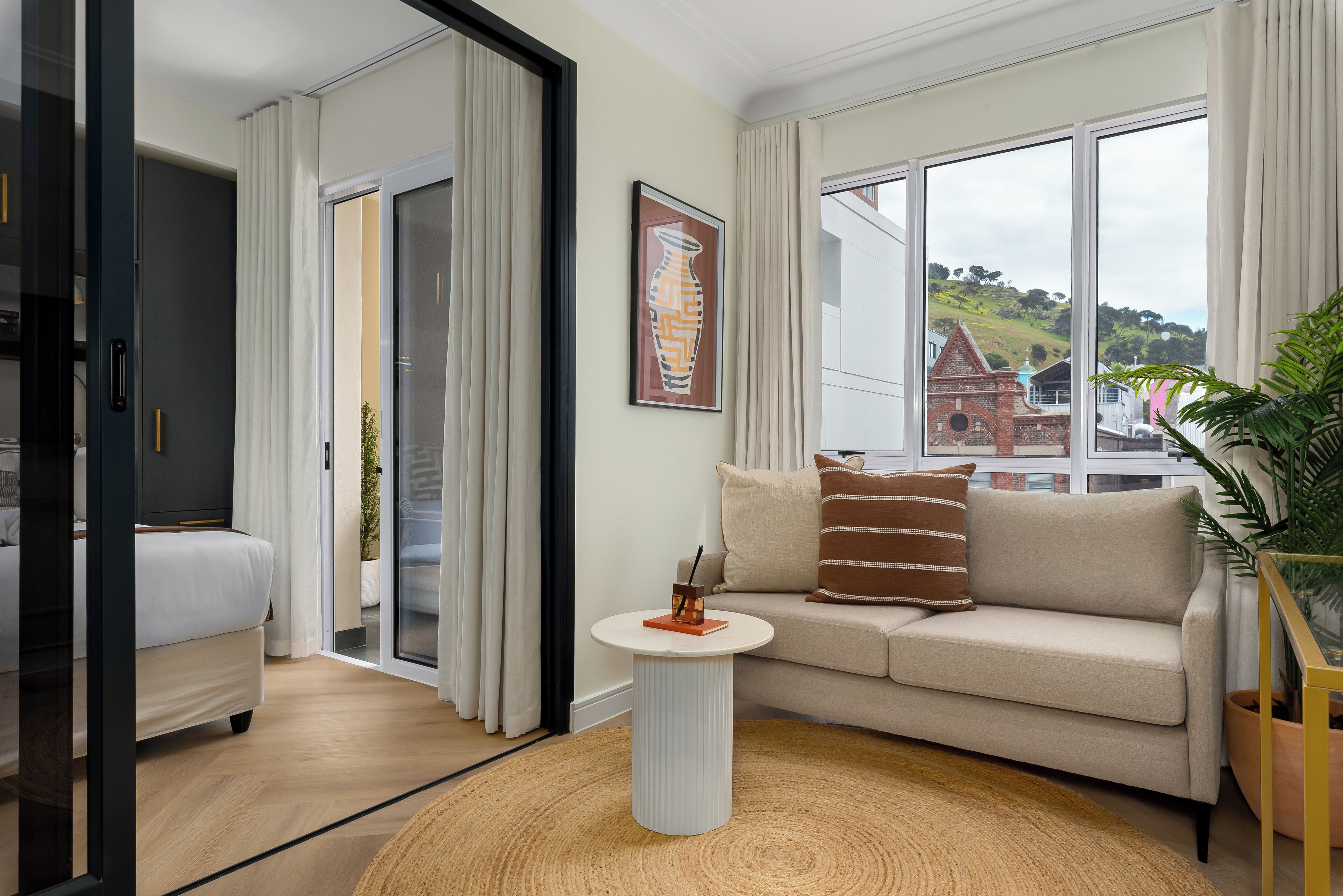 Une chambre d’hôtel moderne, dotée d’un canapé, d’une petite table ronde et offrant une vue sur un immeuble grâce à de grandes fenêtres.