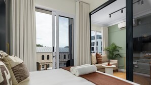 A hotel room with a large bed, a small table, a sofa, and a view of buildings through the window. - The Valour Charming Apartment | City and Hill Views (Cape Town)