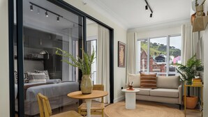 A modern living room with a large bed, a sofa, a coffee table, and a view of a hill and buildings. - The Valour Charming Apartment | City and Hill Views (Cape Town)