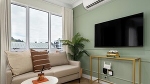 A living room with a sofa, a coffee table, a TV mounted on the wall, and a small side table with books. - The Valour Charming Apartment | City and Hill Views (Cape Town)