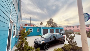 A black car parked in front of a blue building with two garage doors, a sign reading "Votron," and a palm tree in the background. - Blue wave 2 minute walk to beach (Daytona Beach)