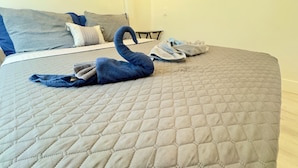 A bed with a quilted grey bedspread, a blue towel shaped like a swan, and a pair of grey slippers. - Blue wave 2 minute walk to beach (Daytona Beach)