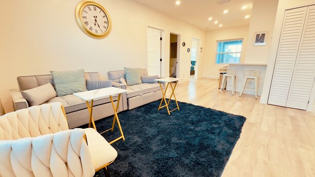A modern living room with a sofa, a small table, a dark blue rug, and a wall clock. - Blue wave 2 minute walk to beach (Daytona Beach)