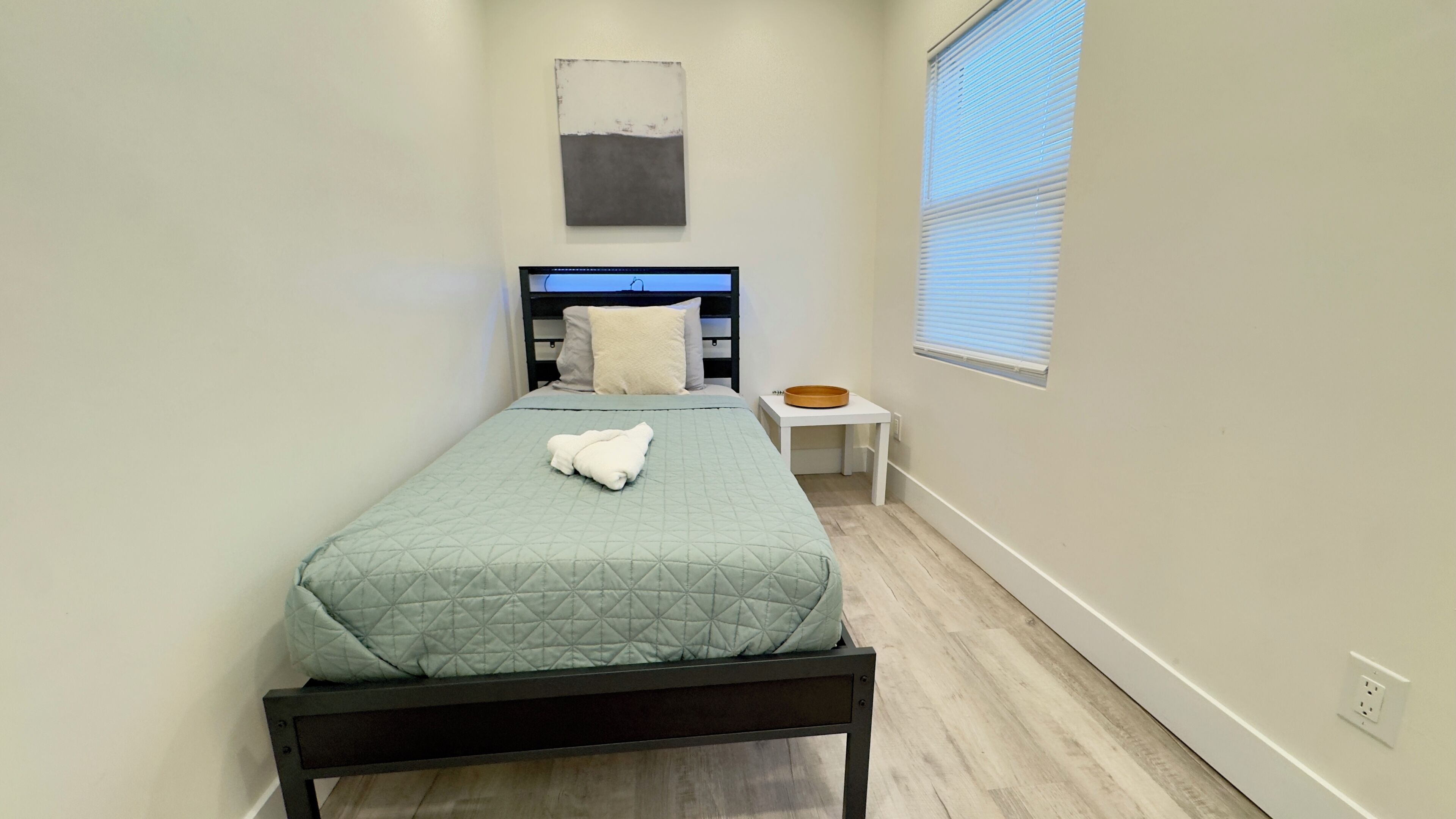 A neatly arranged bedroom with a bed, a bedside table, and a window with blinds.