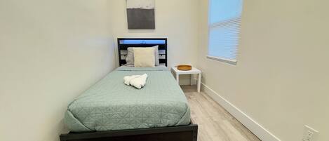A neatly arranged bedroom with a bed, a bedside table, and a window with blinds.