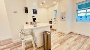 A modern kitchen with a white countertop, a stainless steel trash bin, and a white chair. - Blue wave 2 minute walk to beach (Daytona Beach)