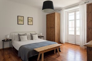 A bedroom with a bed, bedside tables, a wooden bench, a wardrobe, and a window with curtains.