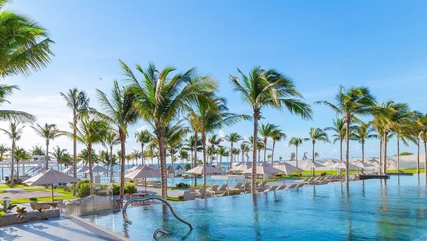 A swimming pool with palm trees and lounge chairs, surrounded by umbrellas and a clear sky. - 3-bedroom condo in enchanting Cancún with fitness room, AC (Cancún)