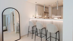 A modern kitchen with a central island, bar stools, pendant lighting, and a large mirror.