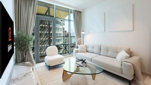 A modern living room with a sofa, armchairs, a glass coffee table, and a TV.