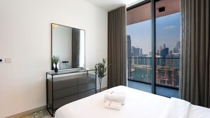 Habitación de hotel moderna con una cama grande, cómoda, espejo y vistas a la ciudad a través de amplias ventanas.
