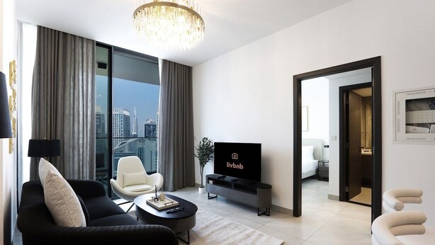 Una sala de estar moderna con un sofá negro, un sillón blanco y un televisor sobre un mueble negro.