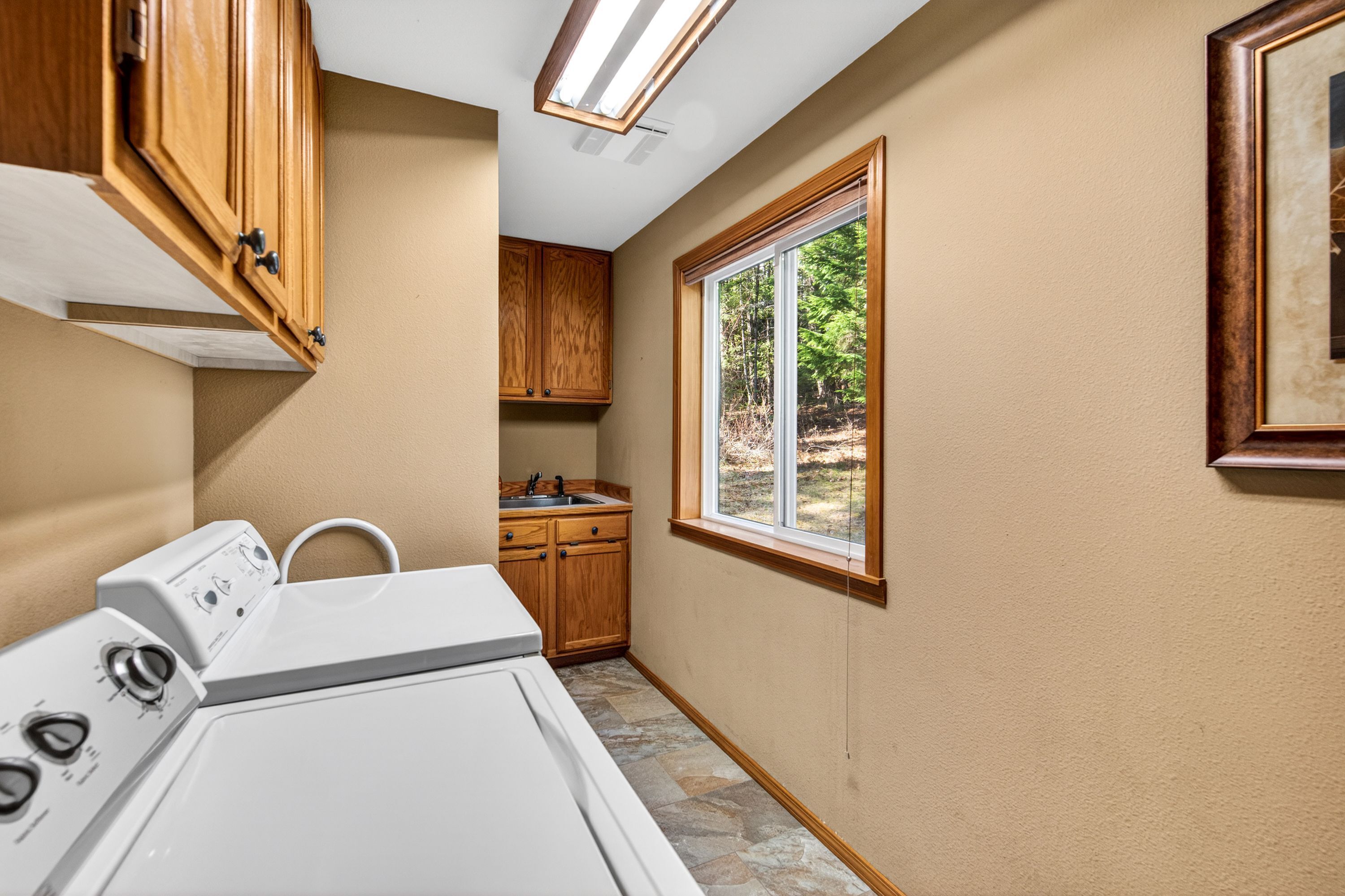 A laundry room with a washer and dryer, wooden cabinets, a window, and a skylight.