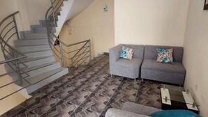 A living area with a grey sofa, a grey armchair, and a glass coffee table. There is a staircase with metal railings leading to an upper floor. The floor has a patterned tile design. - HOTEL CERRO BLANCO (Nazca)