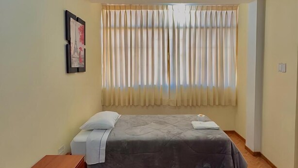 A bedroom with a bed, a wooden dresser, a window with curtains, and a framed picture on the wall. - HOTEL CERRO BLANCO (Nazca)