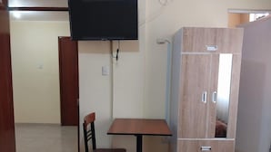 A room with a wooden table and chair, a wardrobe, and a mounted television. - HOTEL CERRO BLANCO (Nazca)