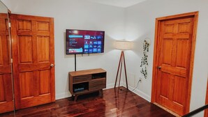 A hallway with wooden doors, a flat-screen TV mounted on the wall, a floor lamp, and a wooden entertainment unit.