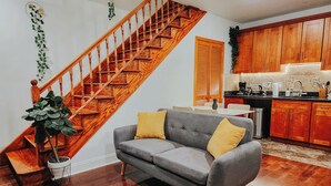 A living room with a grey sofa, wooden staircase, and a kitchen area.