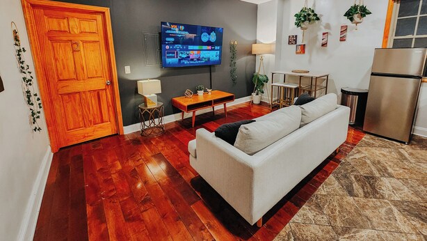 A living room with a wooden door, a TV, a sofa, a small table, and a refrigerator.