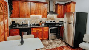 A kitchen with wooden cabinets, a stainless steel refrigerator, a stove, and a dining area with a table and chairs.