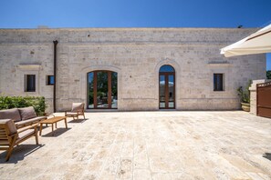 Un bâtiment en pierre doté de fenêtres en arc de cercle et d’une cour aménagée avec du mobilier d’extérieur.