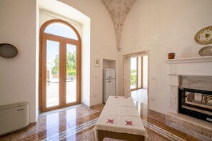 Une pièce dotée d’une grande porte en arc de cercle, d’une cheminée, d’une table recouverte d’une nappe et d’un mur en pierre.