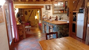 A rustic kitchen with a wooden table, a stone counter, and a white refrigerator. - Apartment in resort center chalet (Chamrousse)