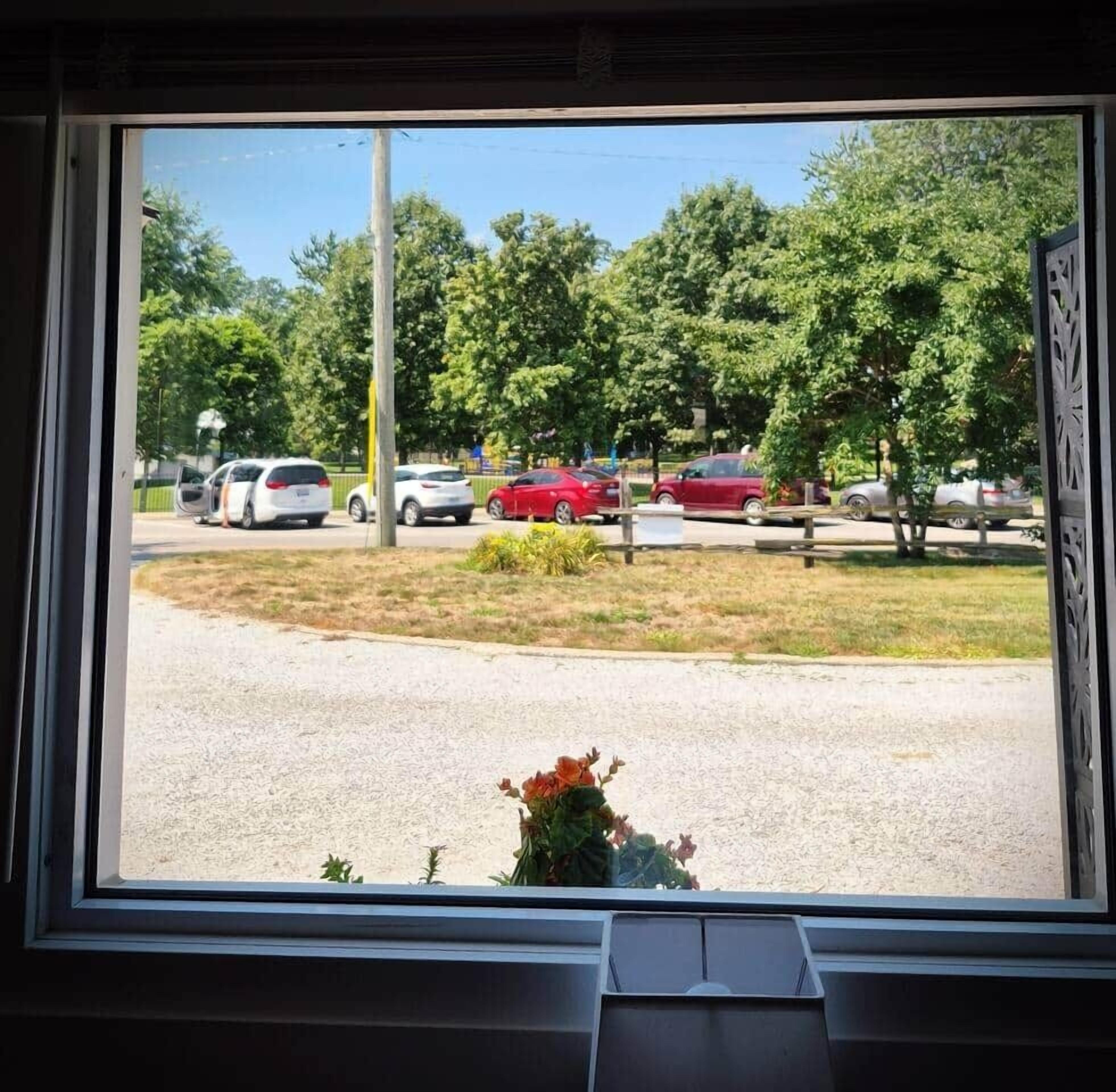 Uitzicht vanuit een gebouw door een raam op een parkeerplaats met auto's en bomen.