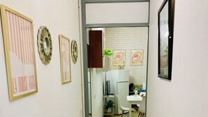 Un corridoio stretto con un termosifone, una porta bianca che dà su una stanza con una scrivania e una sedia, e quadri appesi alle pareti.
