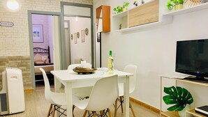 Un soggiorno moderno con angolo pranzo, televisione e una piccola pianta su uno scaffale.