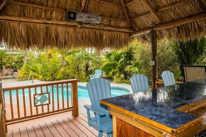 A covered outdoor area with a pool, wooden deck, and blue chairs. - Beautiful 2 Bedroom Pool Home On Big Pine Key (Big Pine Key)