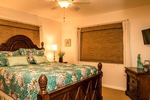 A bedroom with a large bed, a nightstand, a lamp, a potted plant, and a television on the wall.