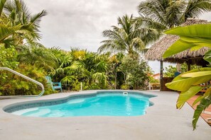 A swimming pool surrounded by lush tropical vegetation and a thatched-roof structure.