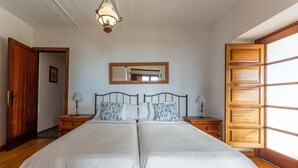 Un lit double avec une tête de lit en bois, deux tables de chevet avec des lampes, un grand miroir au-dessus du lit et une armoire en bois.