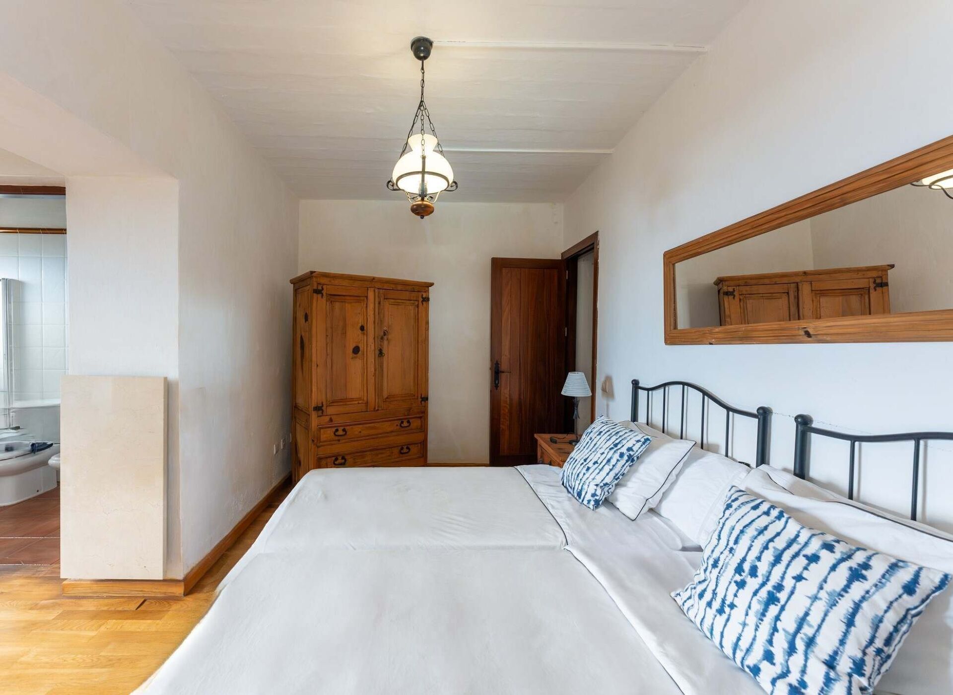 A bedroom with a large bed, wooden wardrobe, and a mirror on the wall.