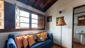Une pièce avec un canapé bleu, des poutres en bois au plafond, un lampadaire et une salle de bain avec un lavabo.