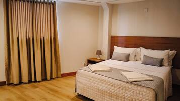 A hotel room with a large bed, a nightstand, a lamp, and a window with curtains.