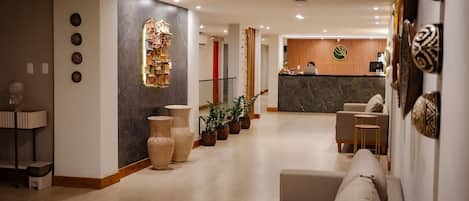 Een hotellobby met een receptiebalie, een bank, potplanten en een decoratief wandkunstwerk.
