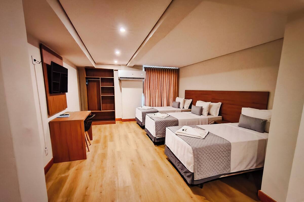Habitación de hotel con tres camas, un escritorio, un armario y televisión.