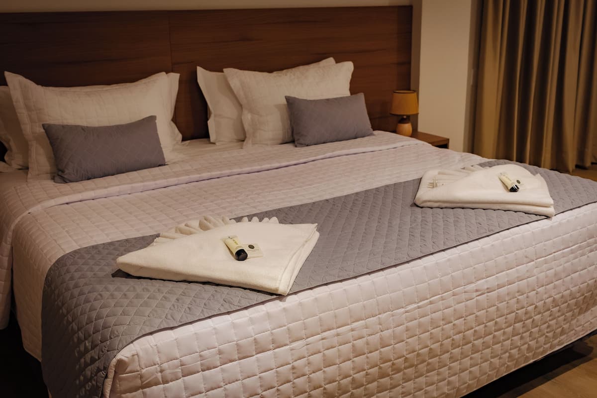 Una cama bien hecha con cubrecama acolchado, almohadas y toallas dobladas.