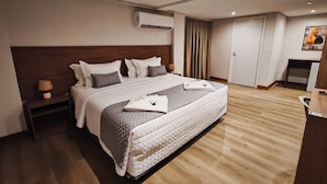 A hotel room with a large bed, a nightstand, an air conditioning unit, a door, and a small desk with a chair. - Amazon Seasons Hotel (Belém)
