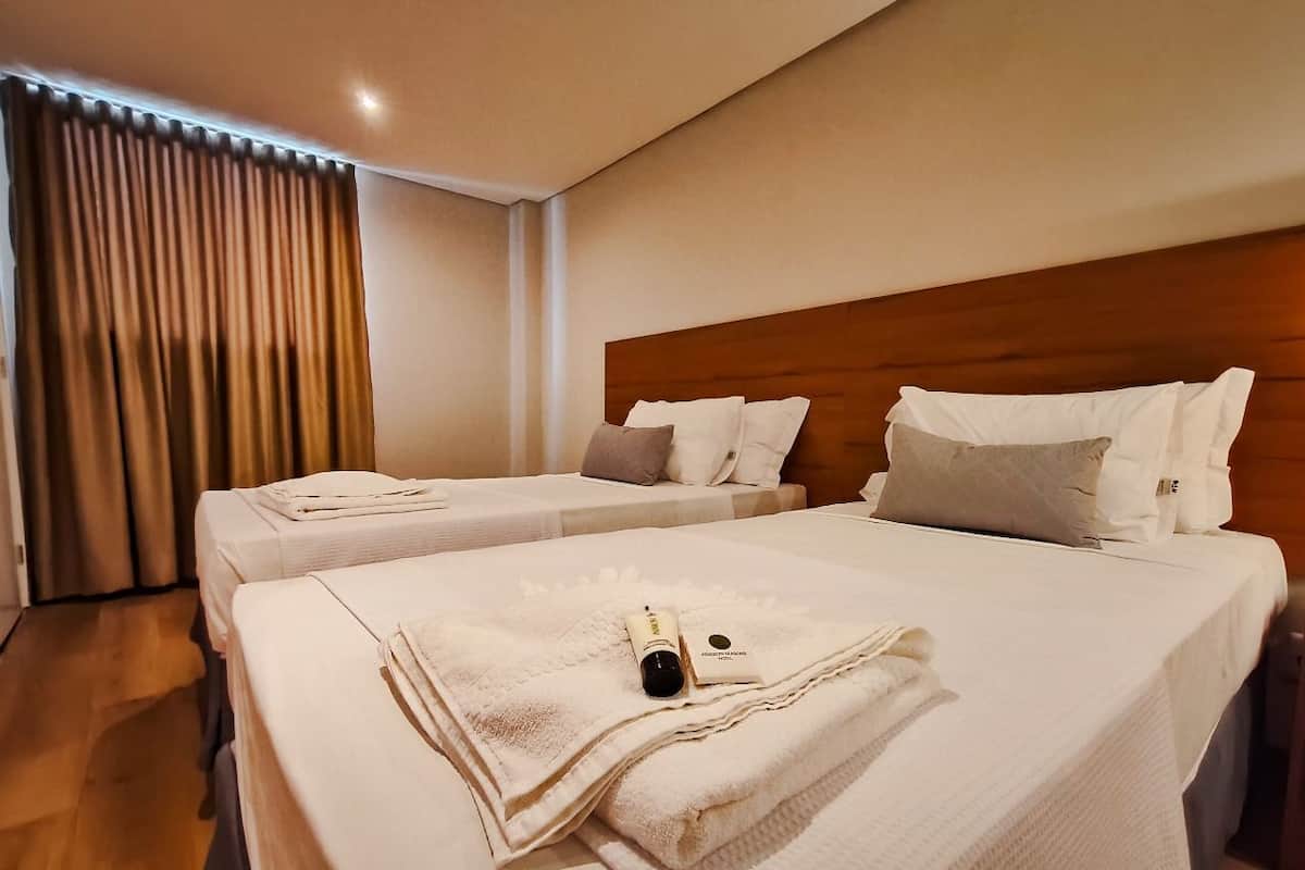 Habitación de hotel con dos camas, cada una con una toalla blanca doblada y una botella de loción.