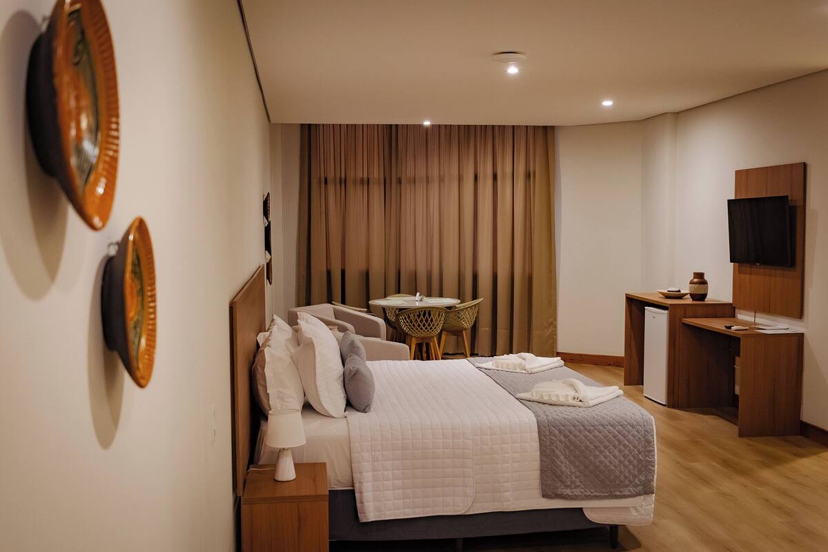 Una habitación de hotel con cama, mesita de noche, lámpara, cortinas, una pequeña mesa y televisión.
