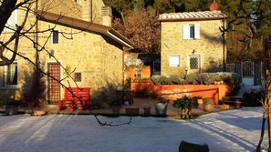 Un edificio de piedra con un banco rojo, plantas en macetas y suelo cubierto de nieve.
