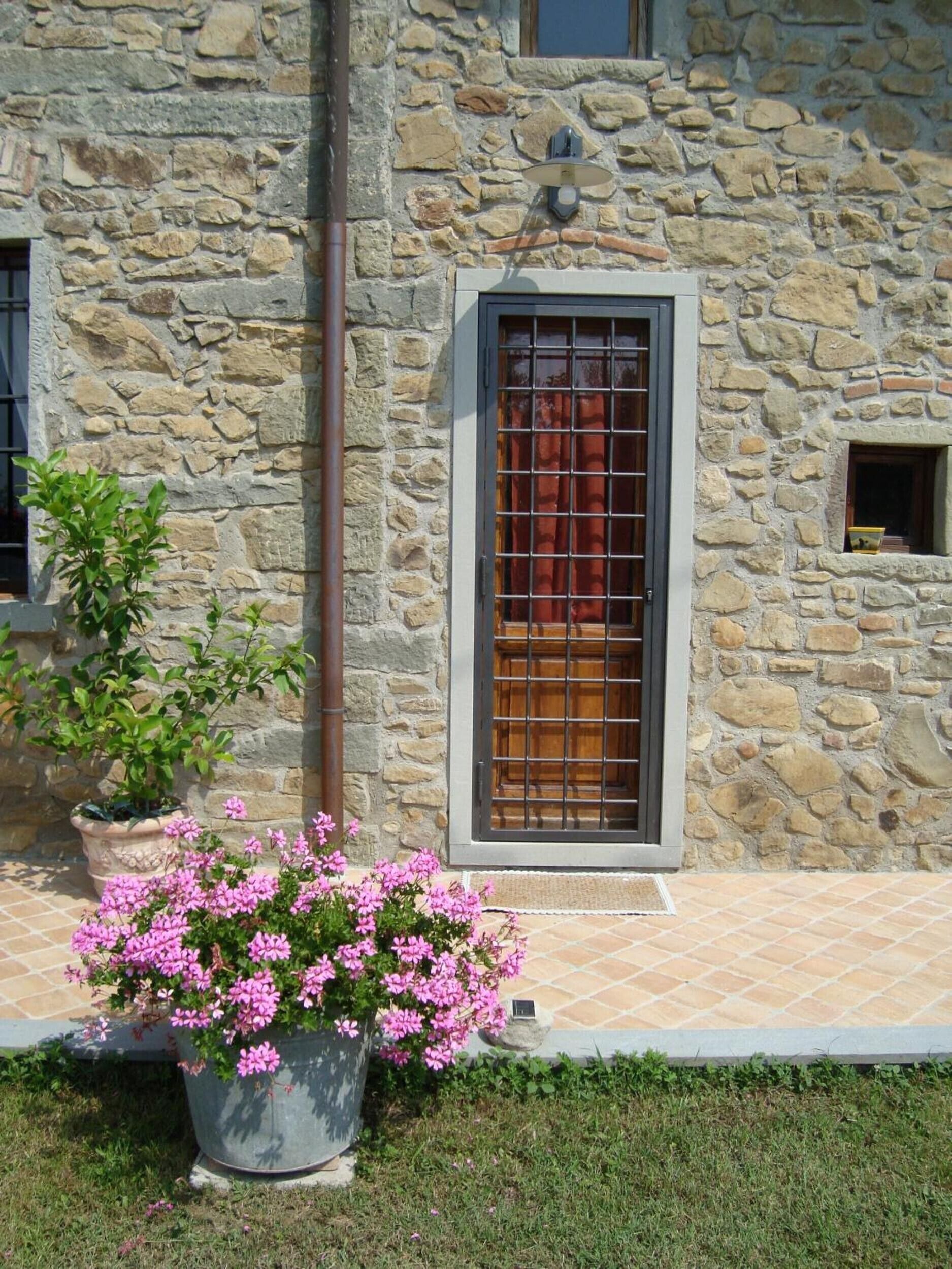 A stone building with a window, a door, and a potted plant with flowers.