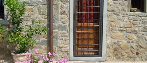 A stone building with a window, a door, and a potted plant with flowers.
